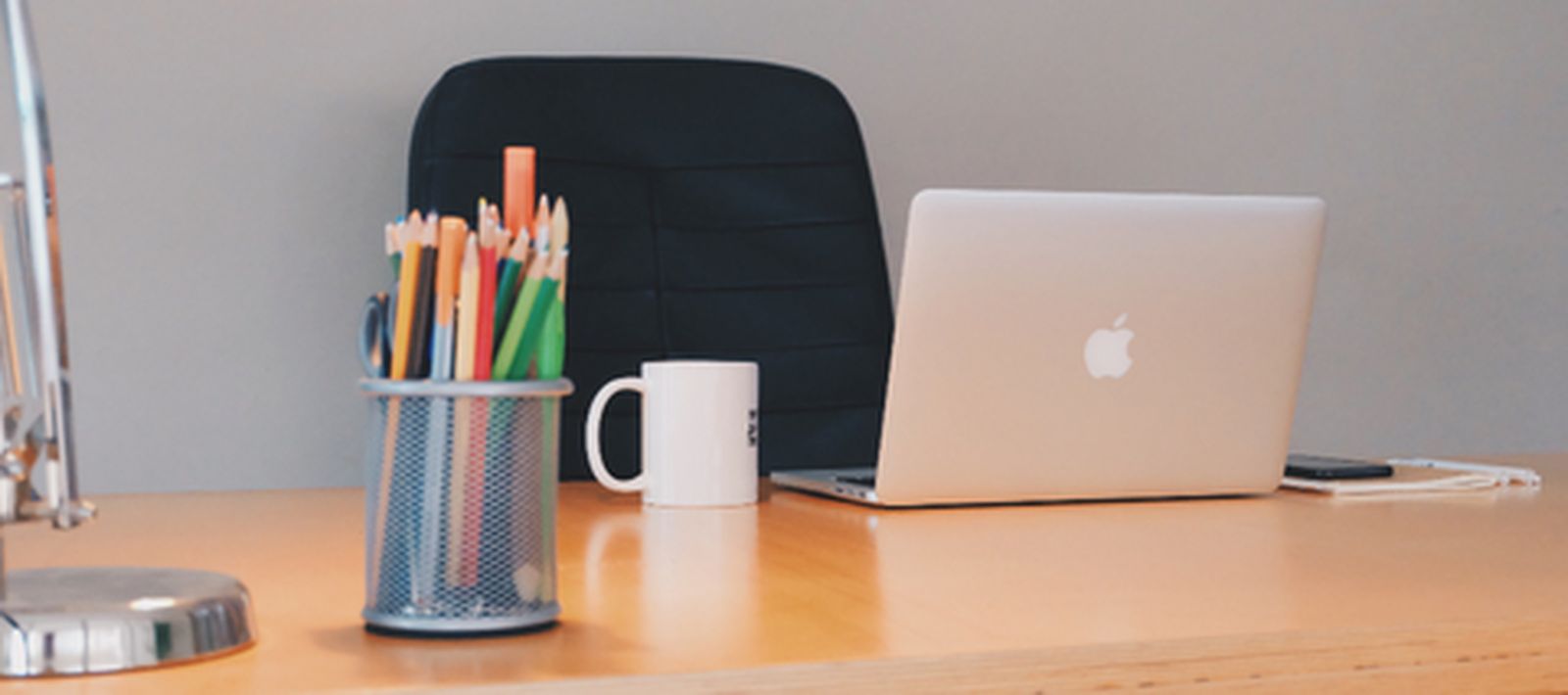 A tidy office desk with a laptop, pencil cup and chair