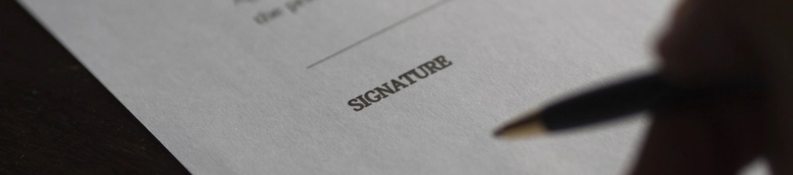 A hand signing a document above a printed signature line